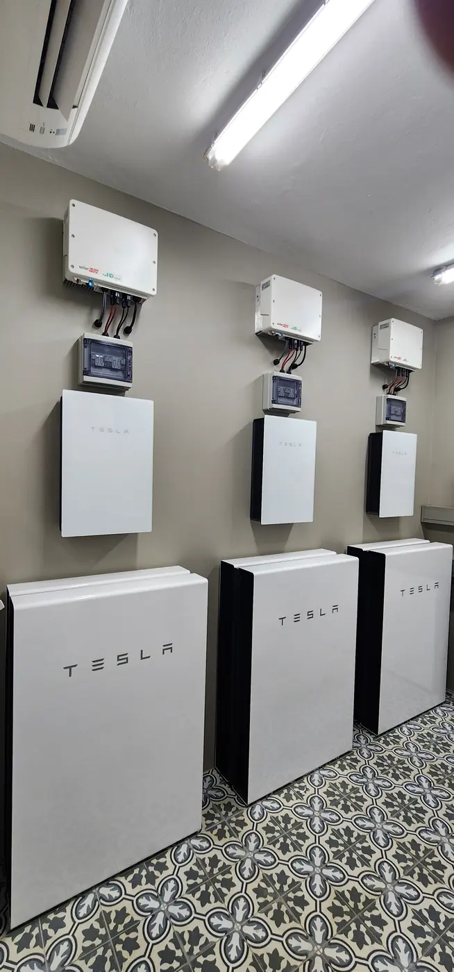 Three Tesla Powerwalls with gateways on a tiled wall
